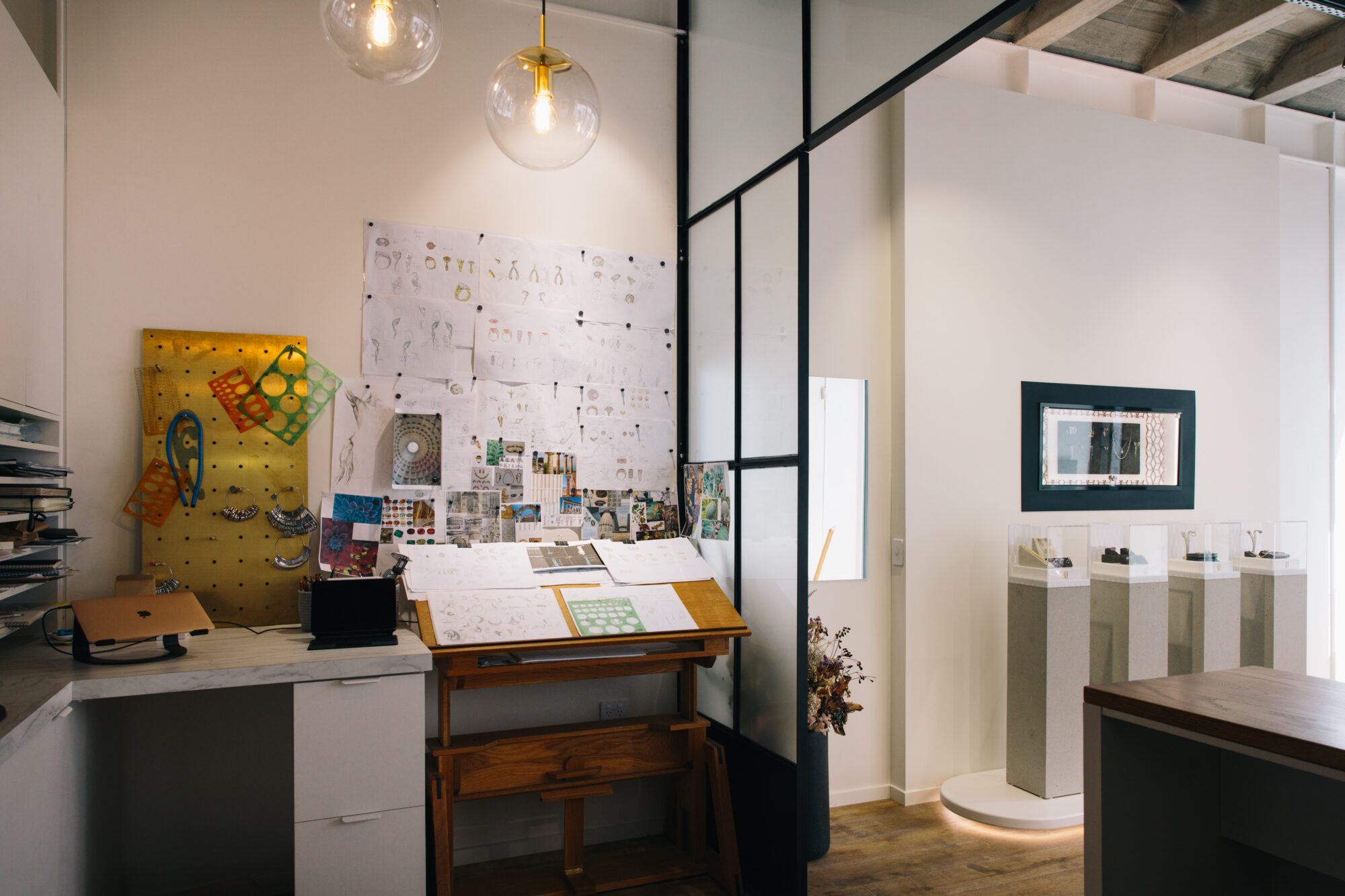 Interior of Alice Herald in Wanaka, showcasing a jewellery design workspace with sketches on the wall, a wooden drafting table, and a display of elegant jewellery pieces on pedestals