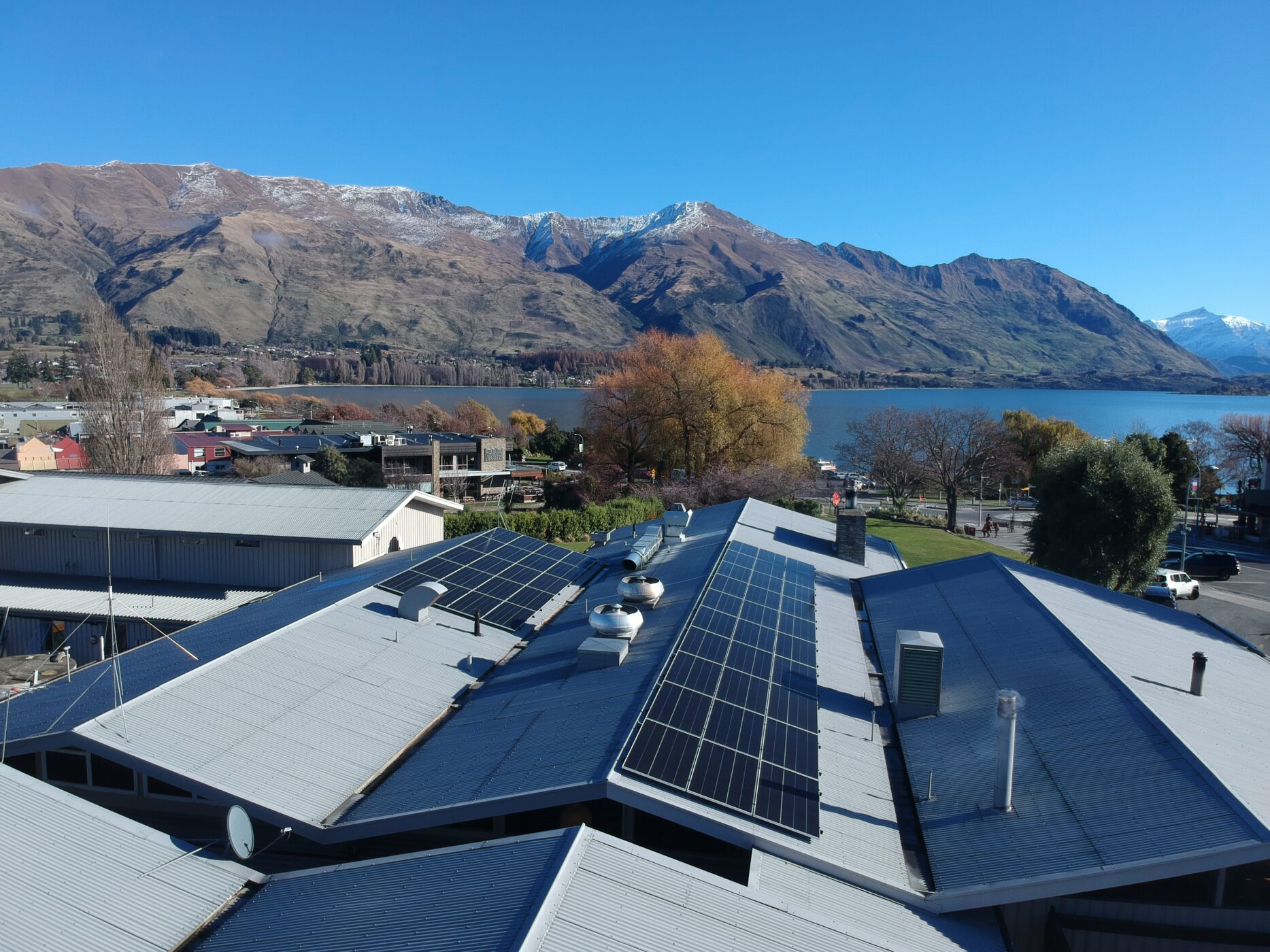The Wānaka Hotel with solar panels installed on its roof, set against Lake Wānaka and surrounding mountains in autumn