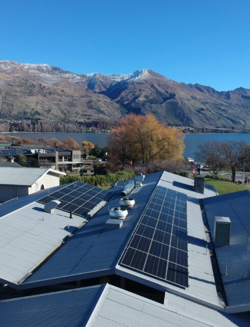 The Wānaka Hotel with solar panels installed on its roof, set against Lake Wānaka and surrounding mountains in autumn