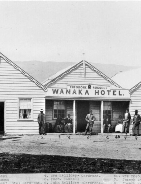 Historical black and white photograph of the original wooden Wānaka Hotel building with people standing outside its entrance.